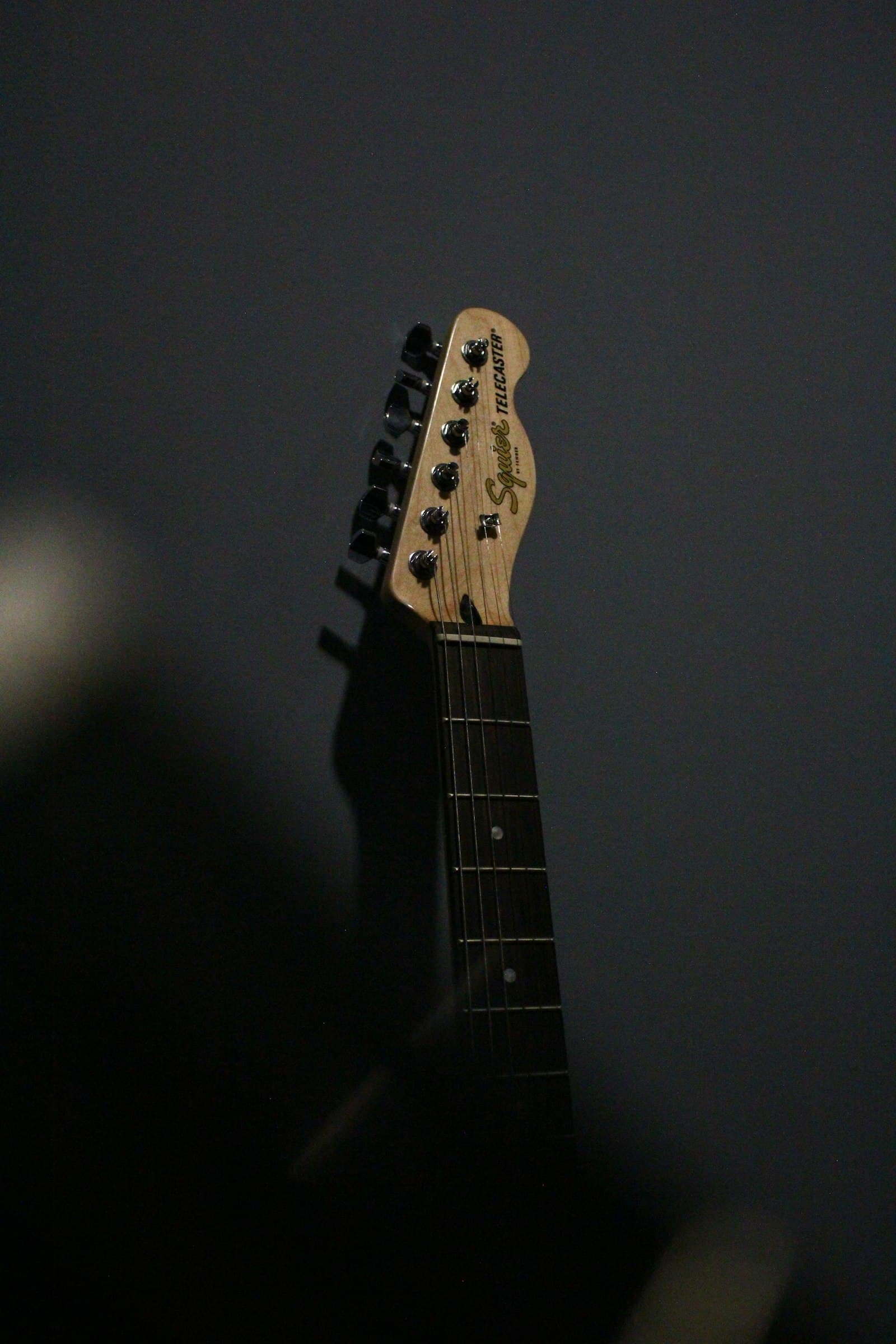 Headstock dan neck gitar elektrik dengan latar gelap